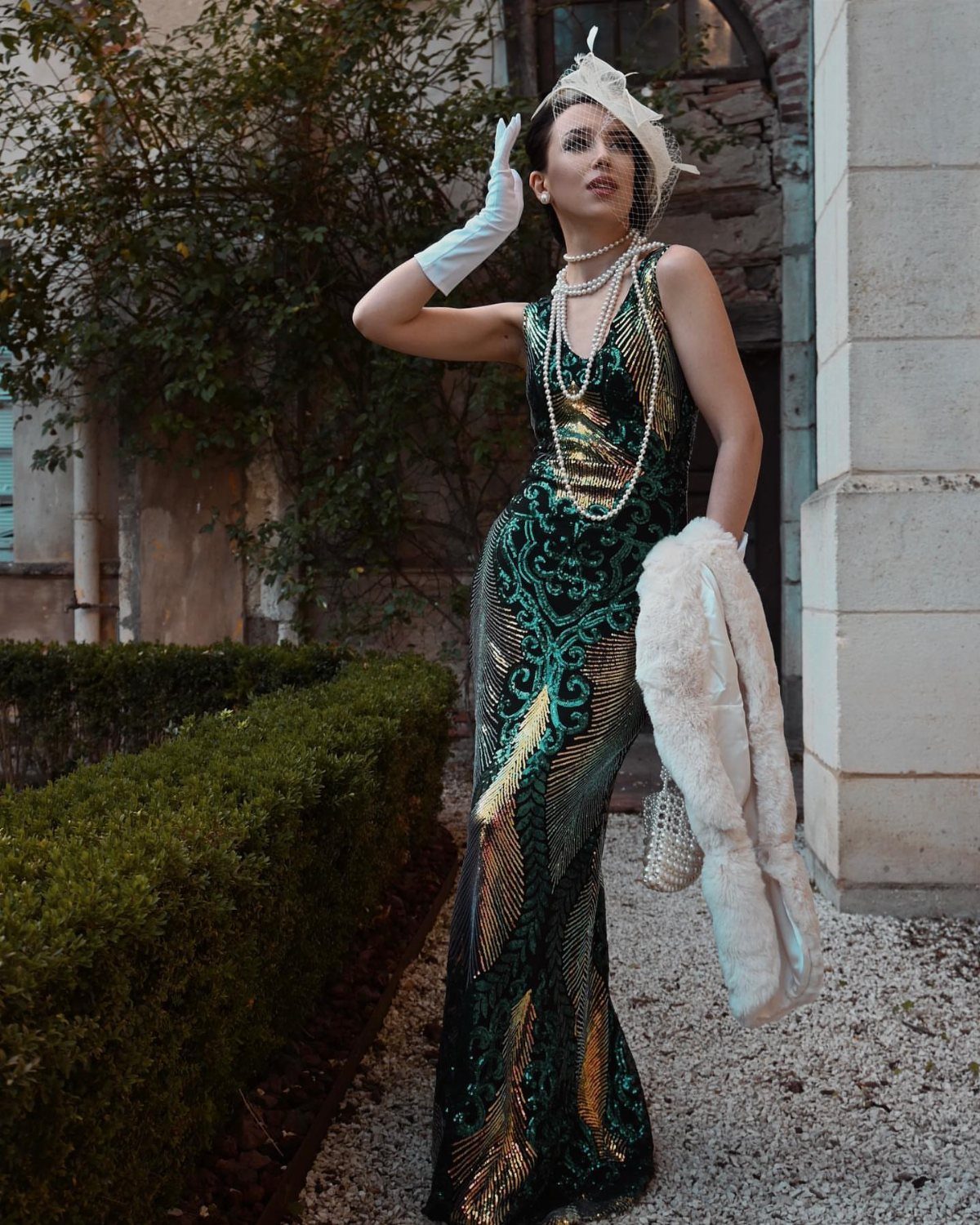 Woman in a green sequined Gatsby-style long dress with pearls and fur stole.