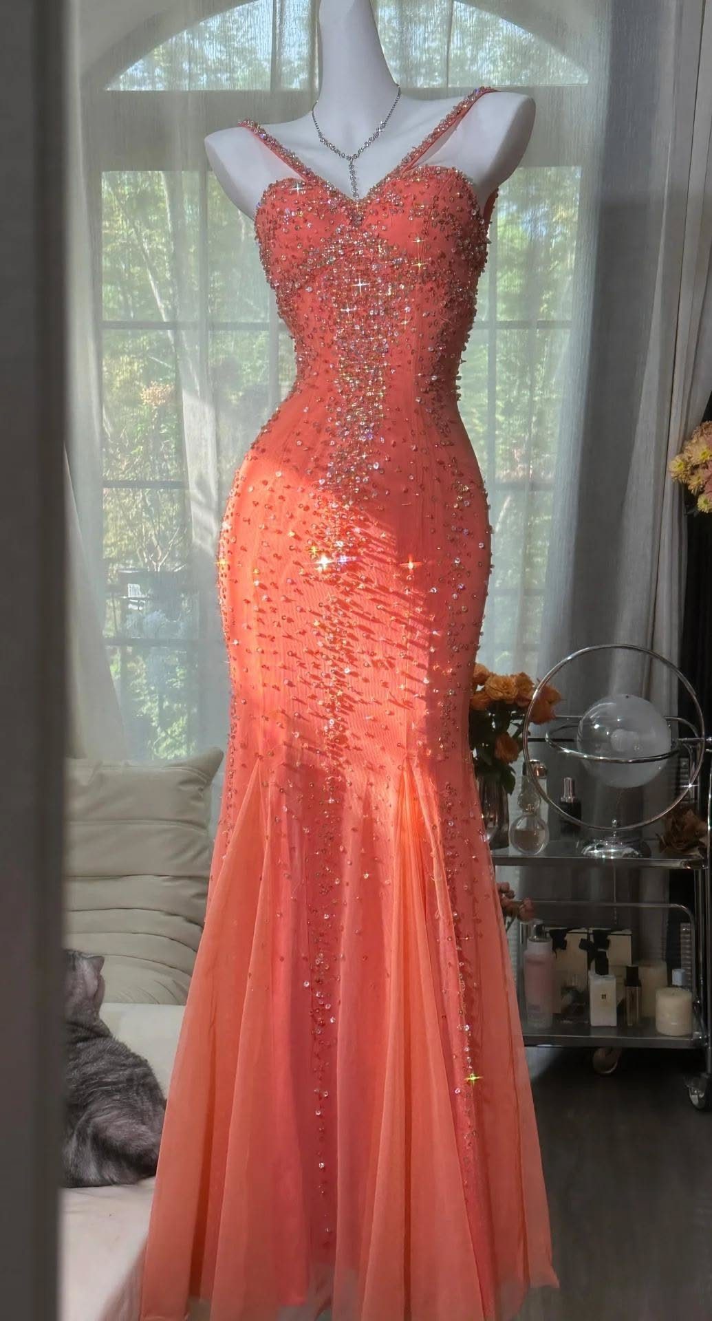 Coral mermaid silhouette gown with sequins and beads on a white mannequin.