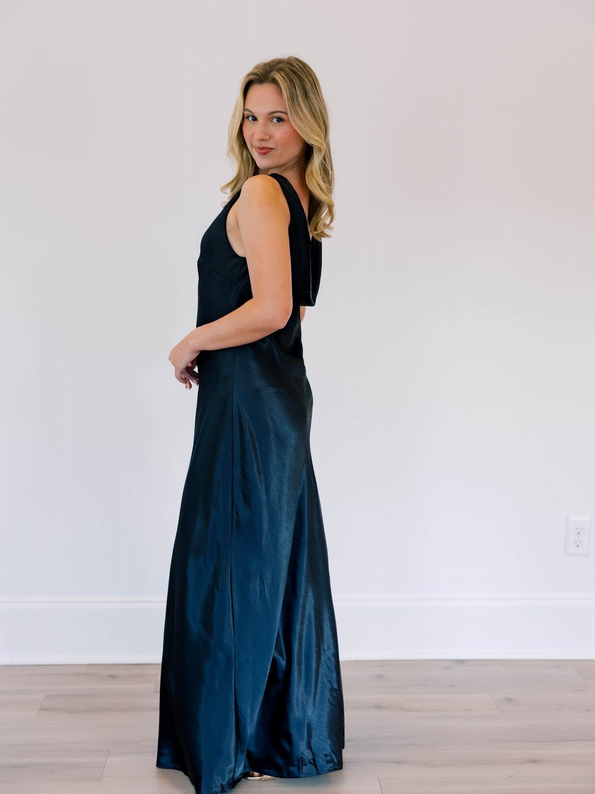 Woman in a long sleeveless black satin evening gown standing against white wall