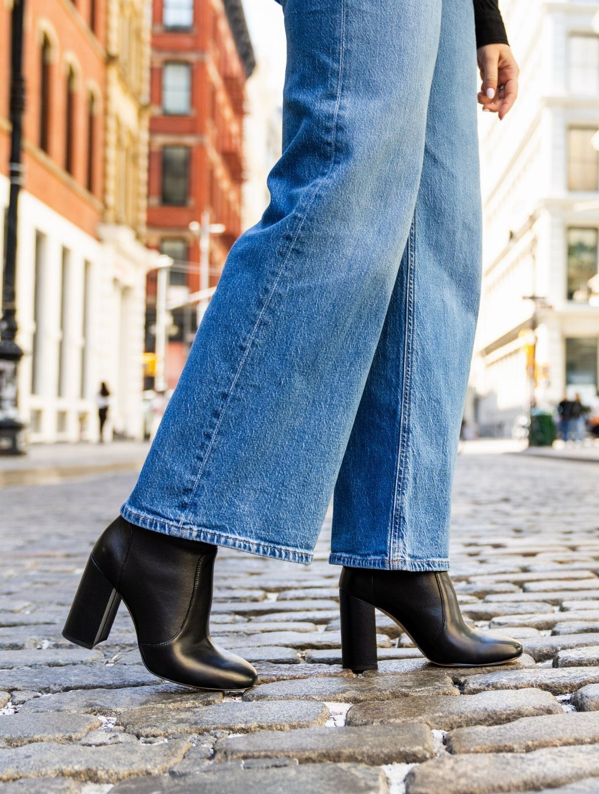 Black leather ankle boots with block heels paired with wide-leg blue jeans.
