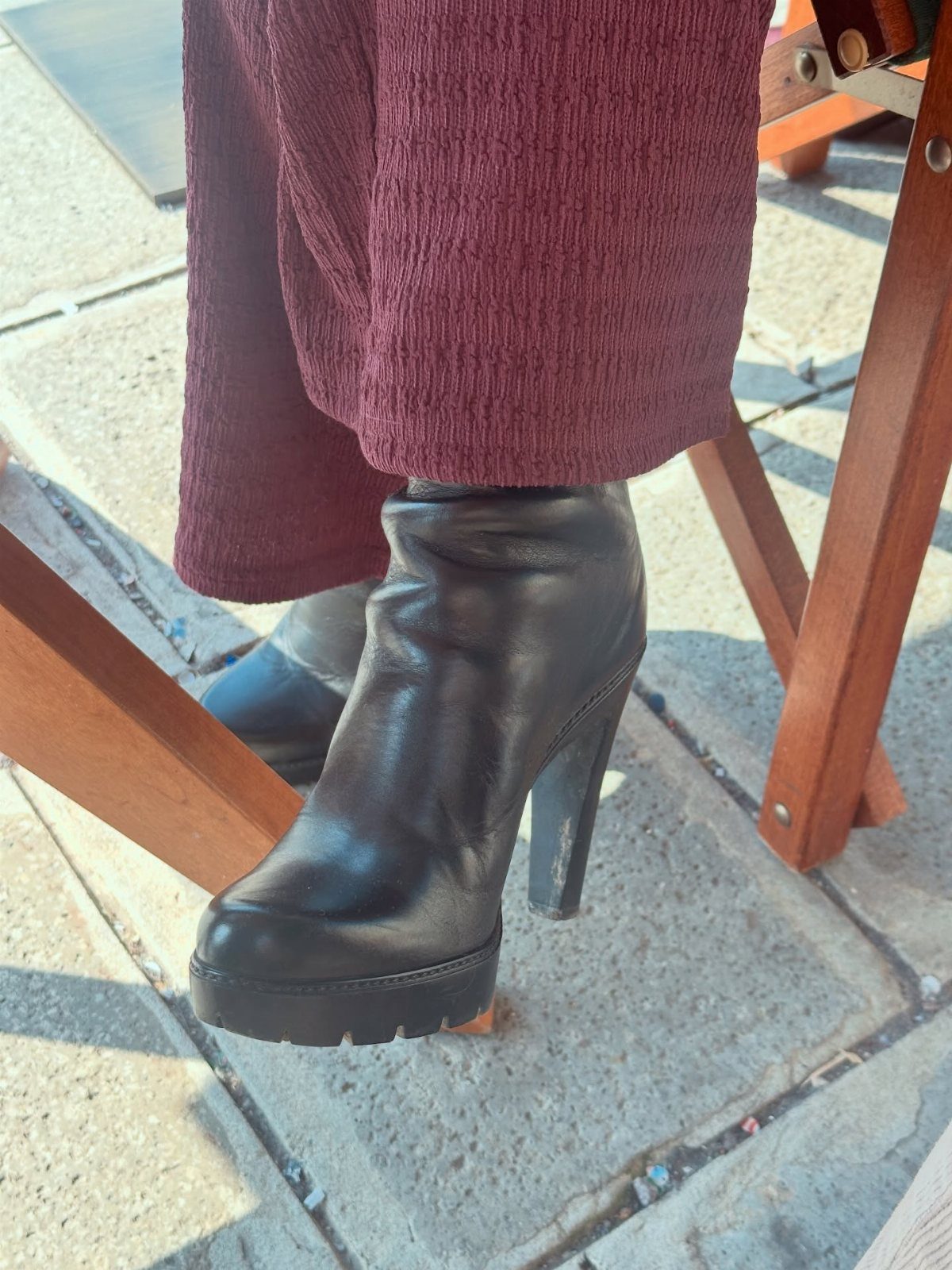 Black leather block heel boots with lug soles and burgundy trousers on pavement