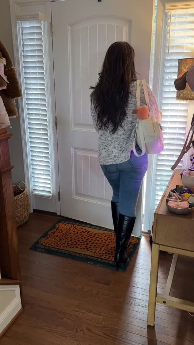Woman wearing tall black leather boots and blue jeans standing by a door.