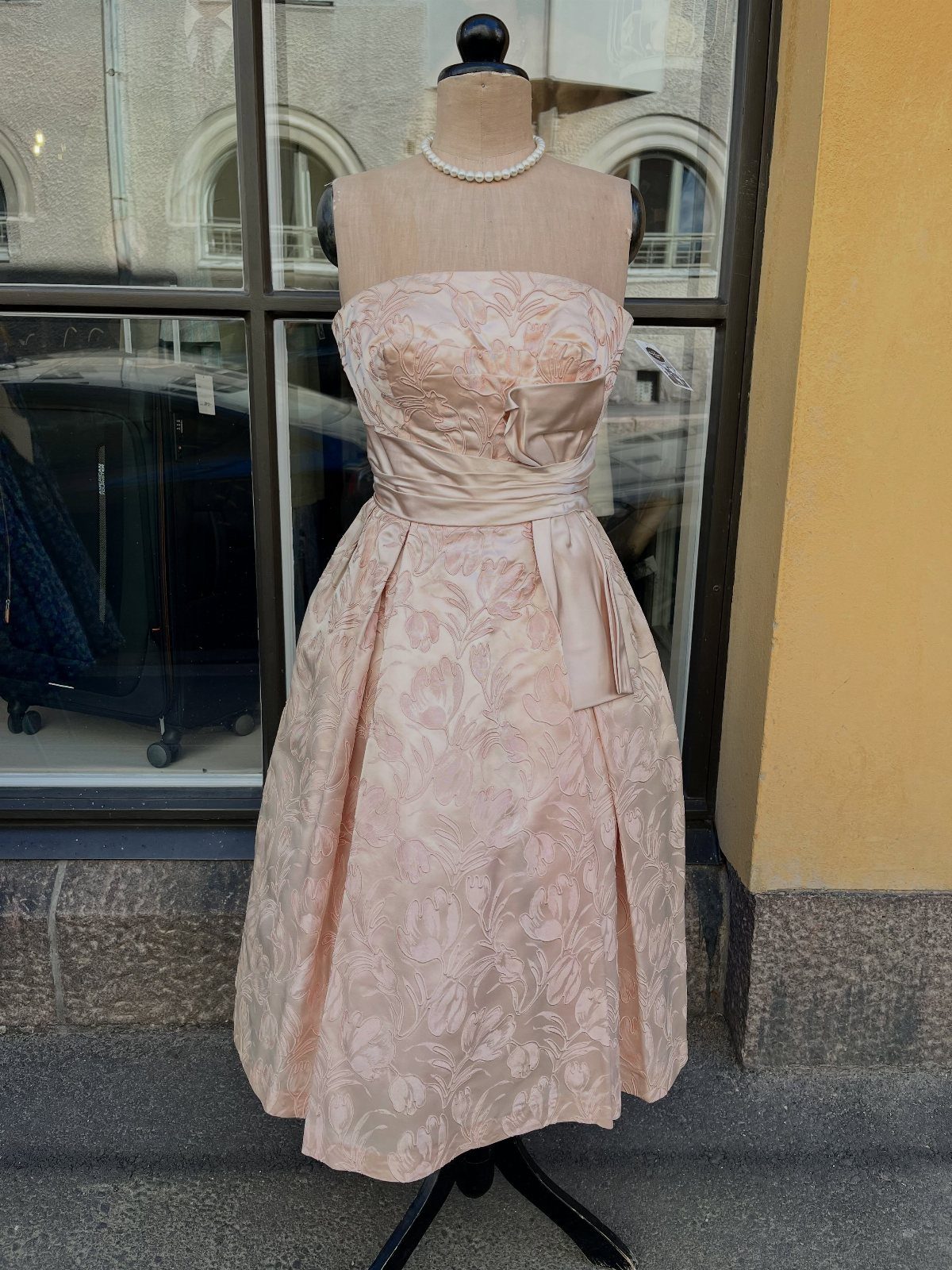 Pale pink floral brocade strapless evening dress on a mannequin with pearl necklace