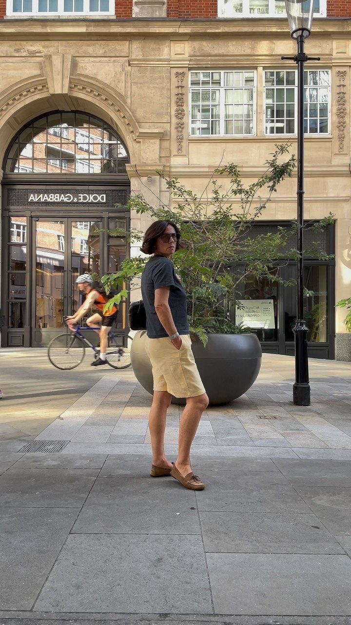 Woman wearing a grey t-shirt and yellow skirt standing on a city street.