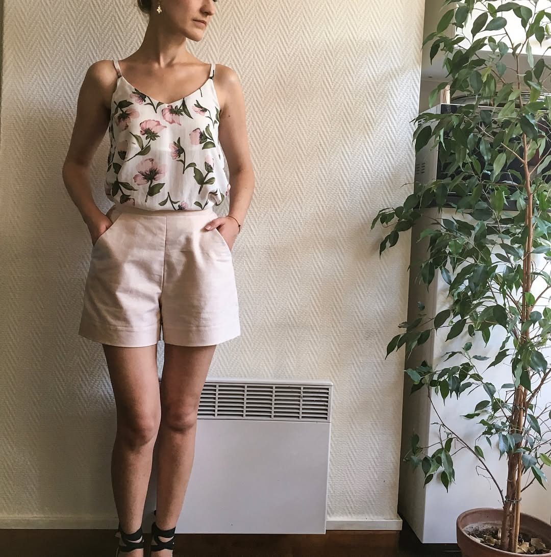 Woman wearing a floral tank top and beige linen shorts standing indoors.