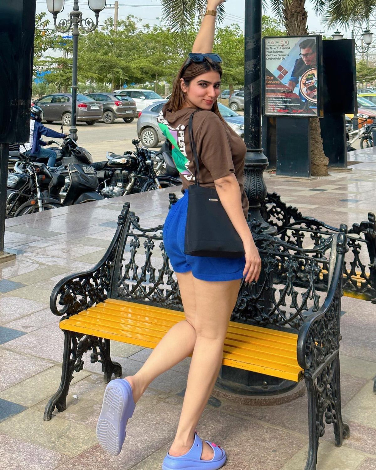 Woman wearing a brown t-shirt and blue shorts standing by a yellow bench.