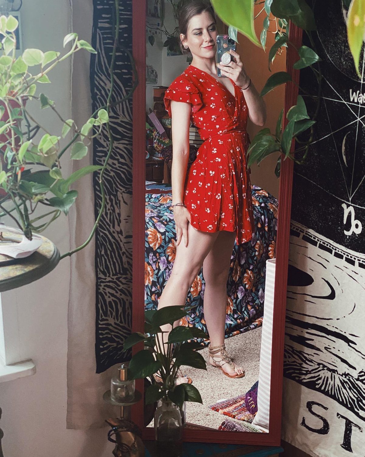 Woman in a red floral sundress and tan flat sandals taking a mirror selfie.