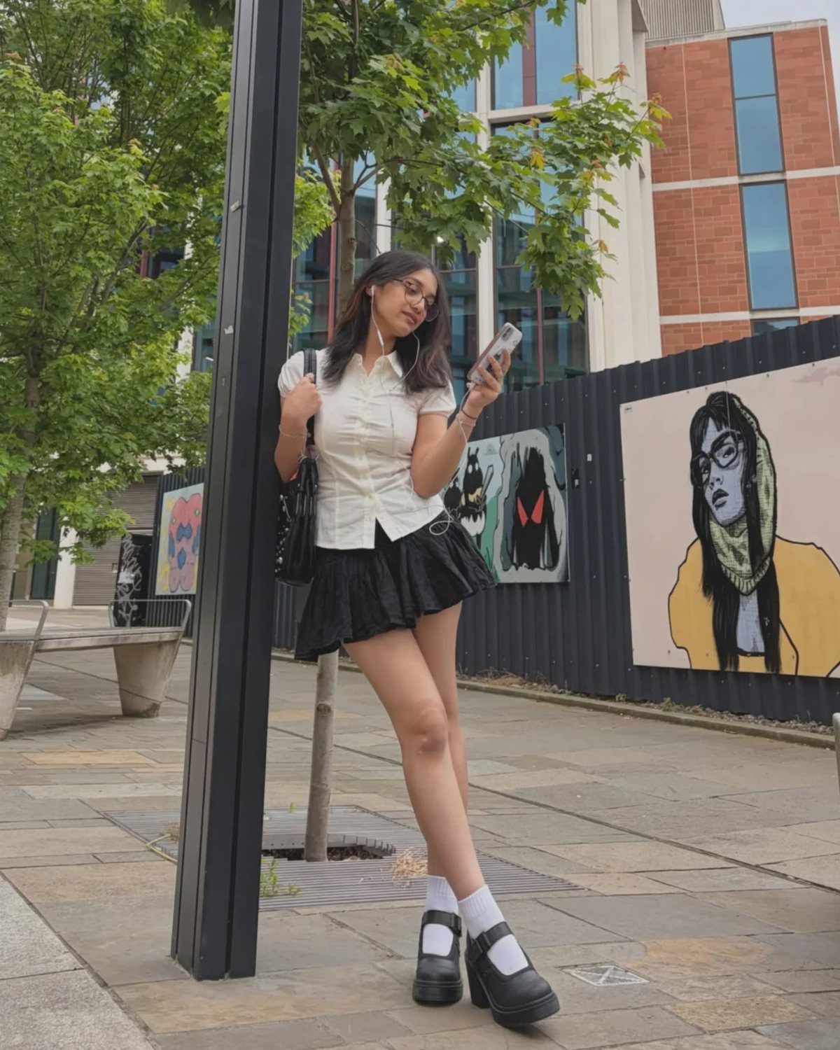 90s Skirt Outfits: 7 Ideas, from Floral Maxi to Mini 5 Woman wearing a white shirt and black pleated mini skirt on a city street