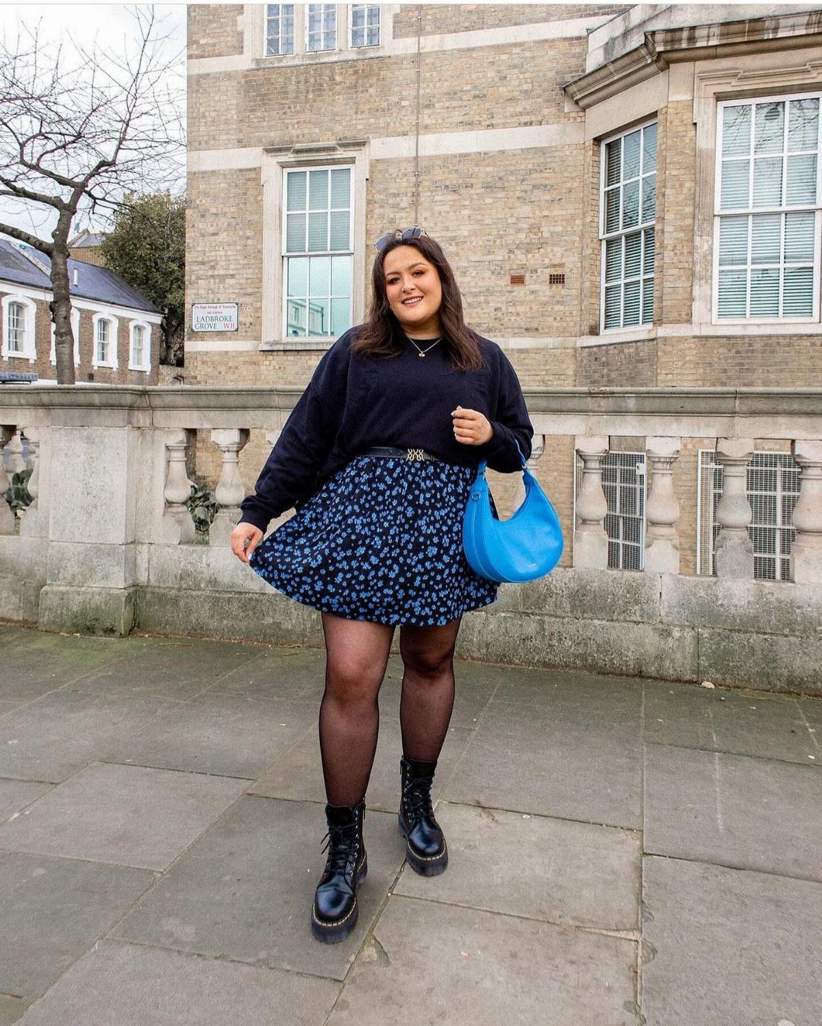 90s Skirt Outfits: 7 Ideas, from Floral Maxi to Mini 7 Woman wearing black chunky boots, a blue floral skirt, and a black sweater.