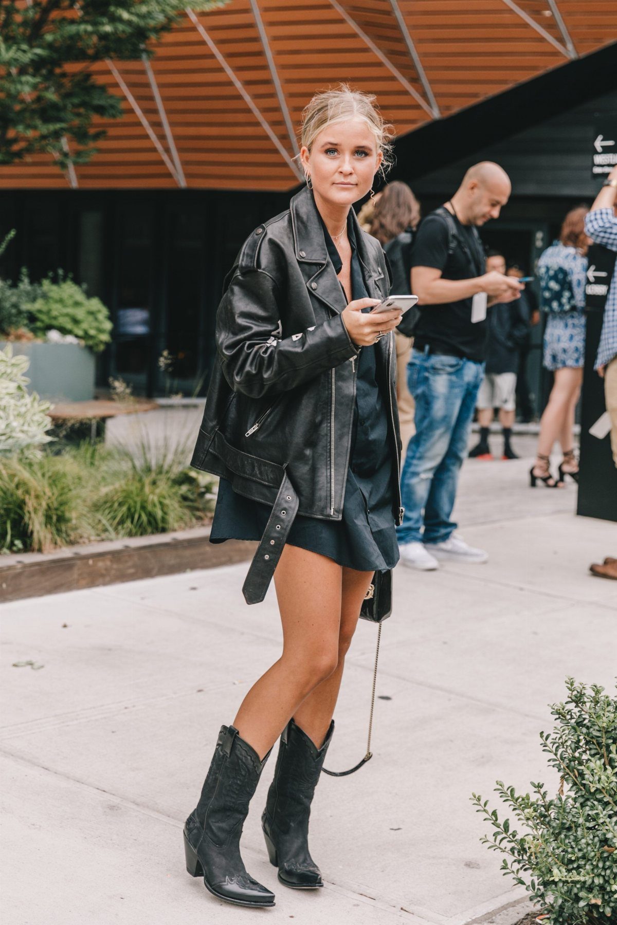 Woman wearing a black leather biker jacket, black mini dress, and black ankle boots.