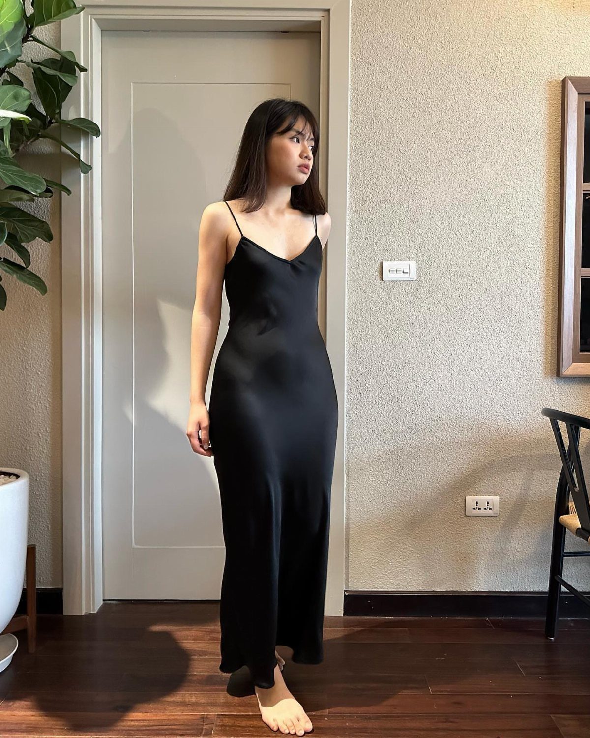 Woman wearing a long black satin slip dress standing in a bright room