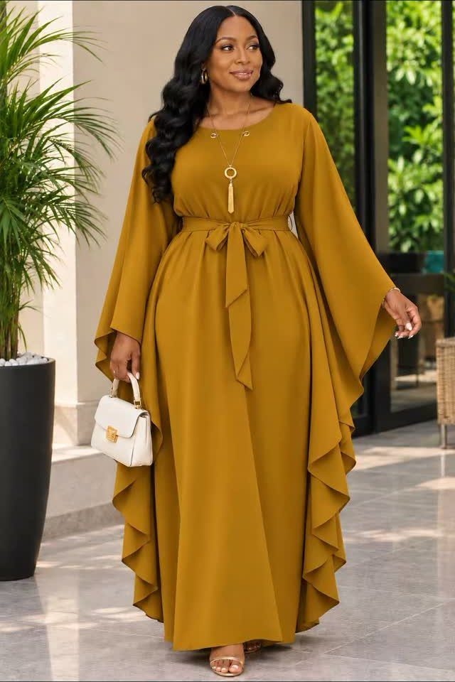 Woman in a mustard-yellow flowy dress with a tie-belt and wide sleeves.