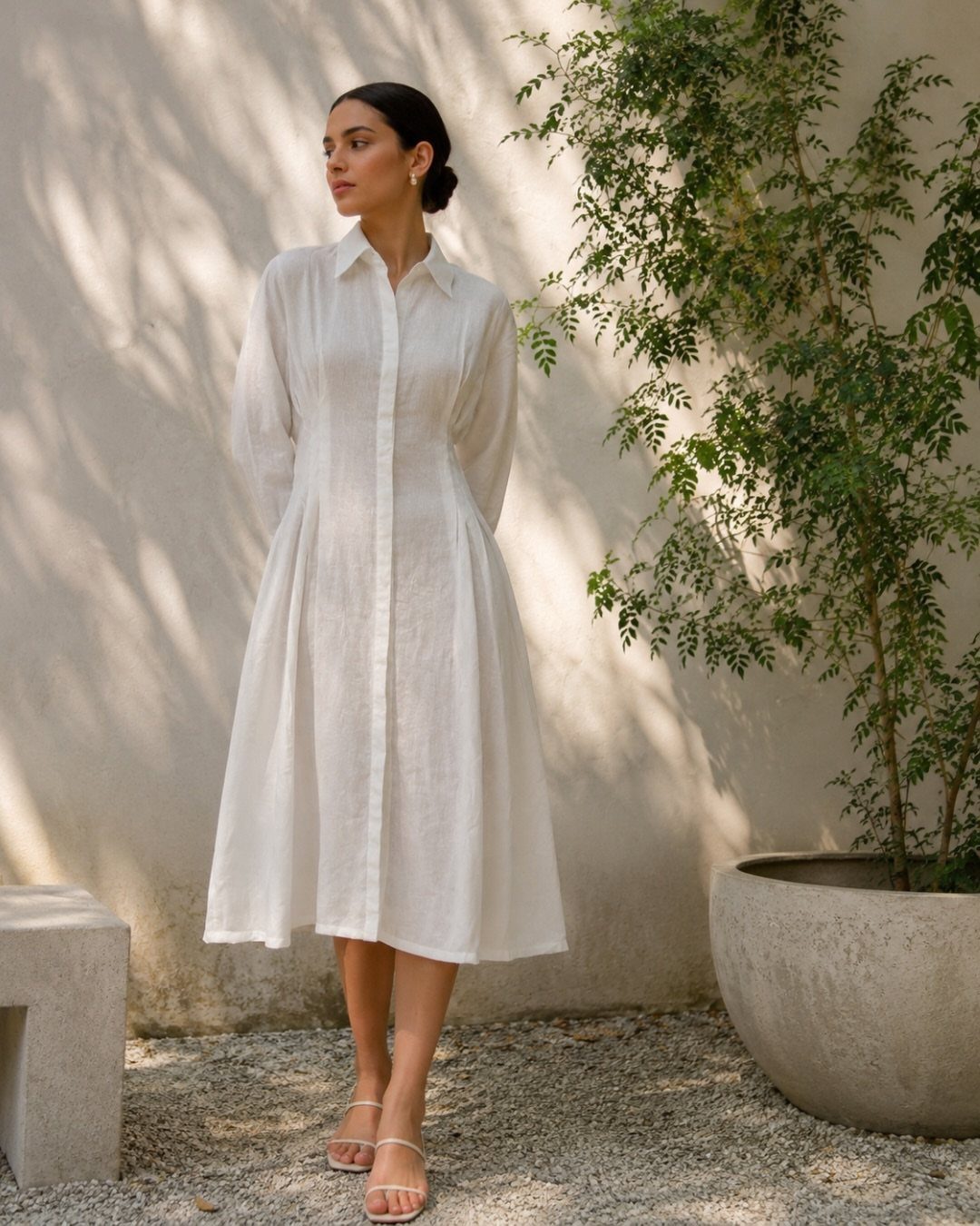 Woman in a white flowy midi dress and strappy sandals standing outdoors.