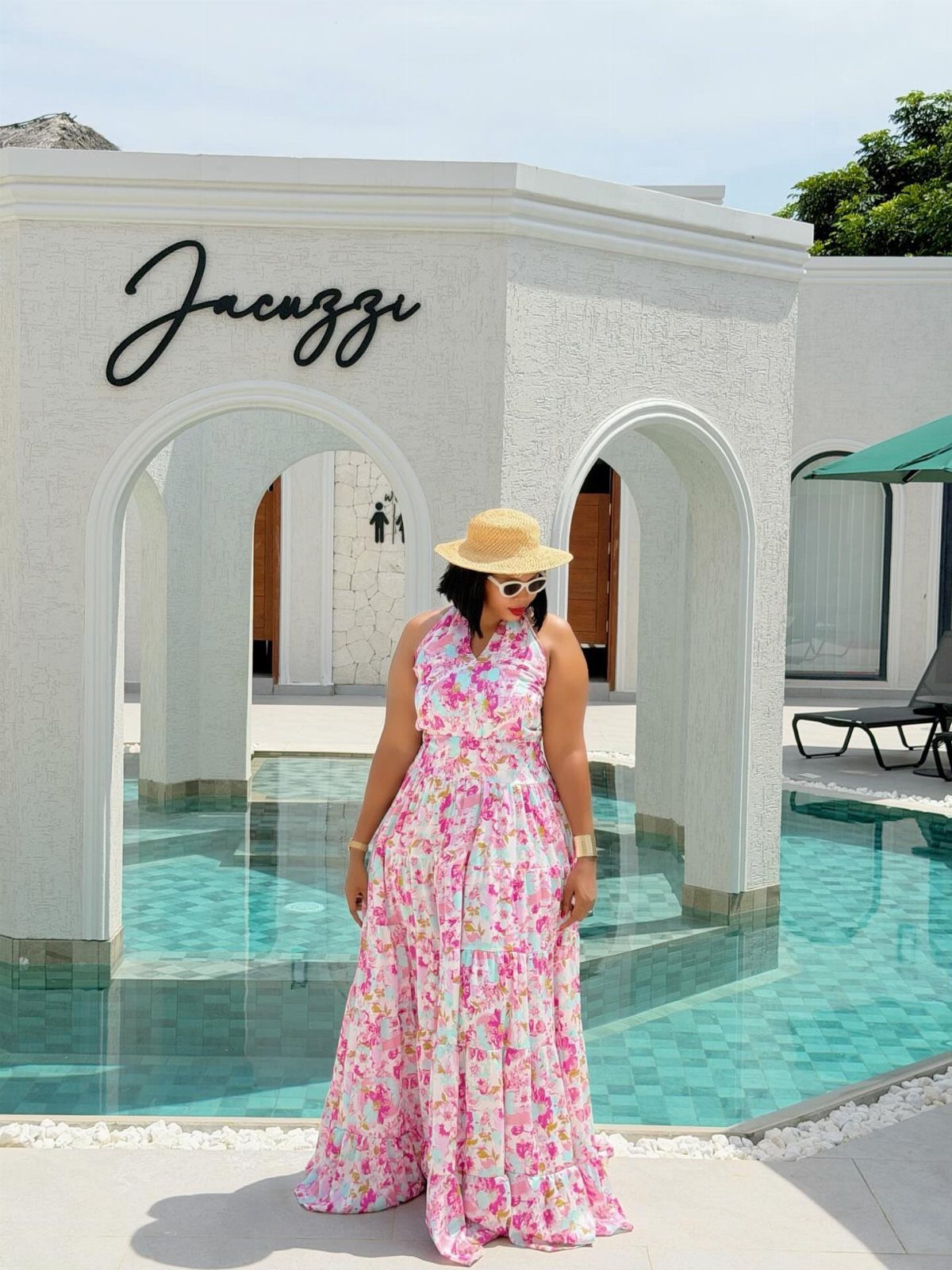Woman in a pink floral tiered flowy dress and straw hat by a pool