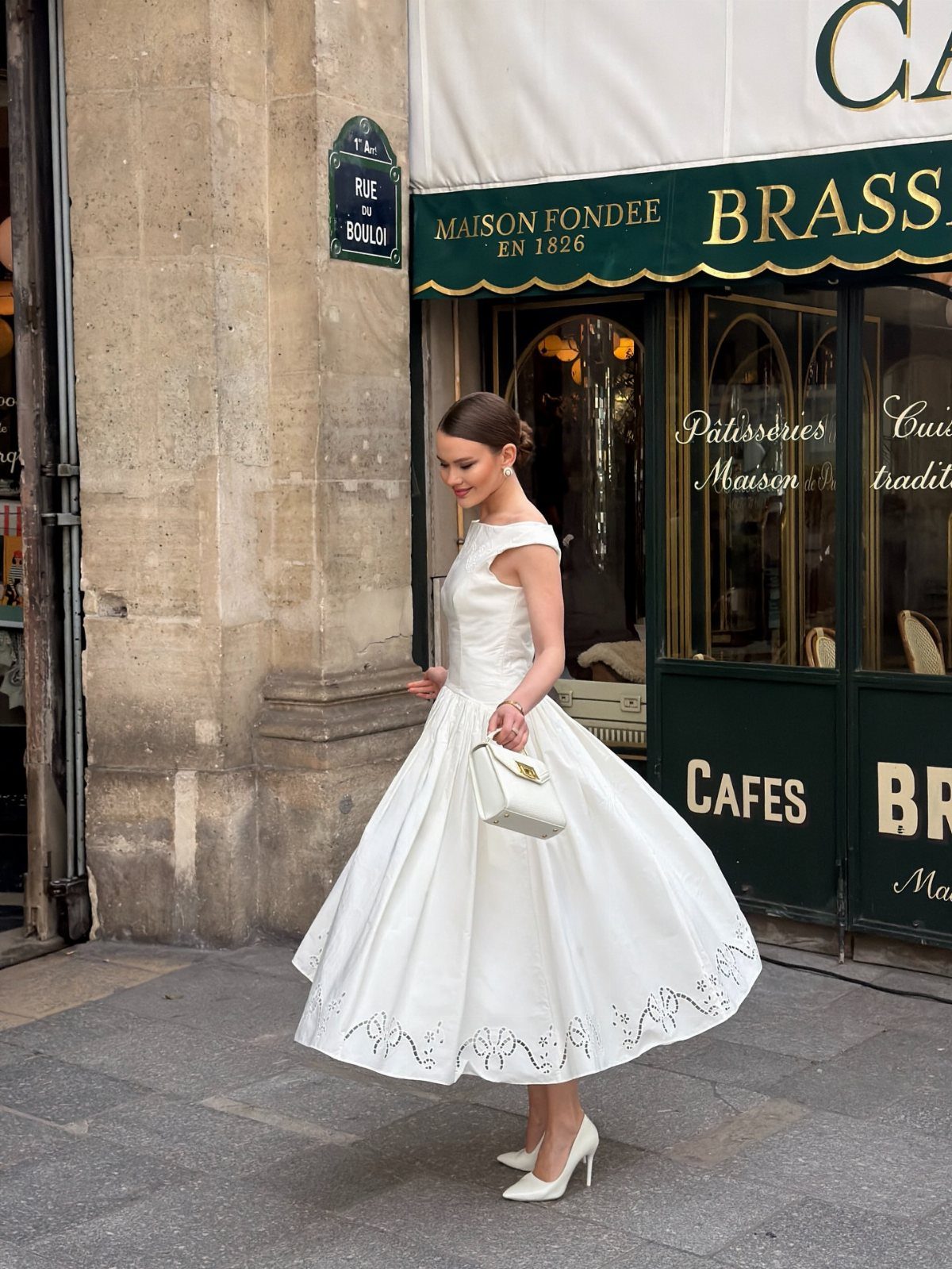 Woman in a white flowy tea-length dress and heels standing by a cafe