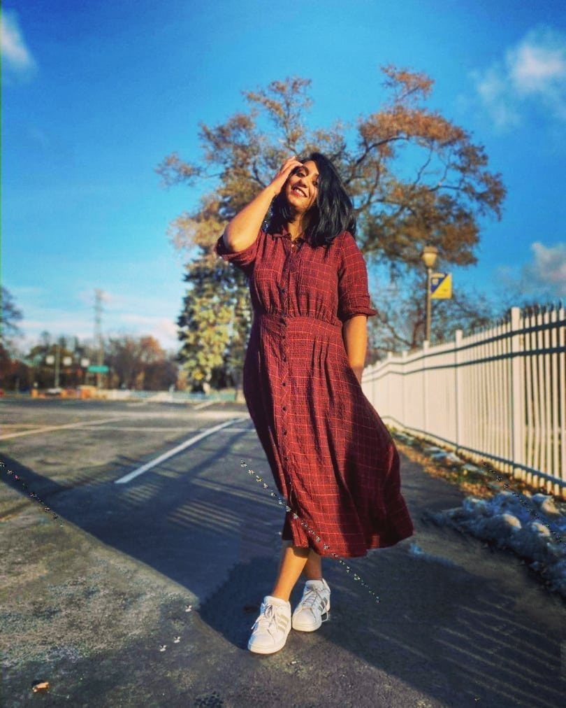 Woman in a red flowy midi dress and white sneakers standing outdoors.