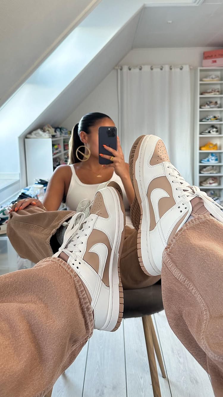 Beige and white Nike Dunk sneakers worn with brown textured trousers in a mirror selfie.