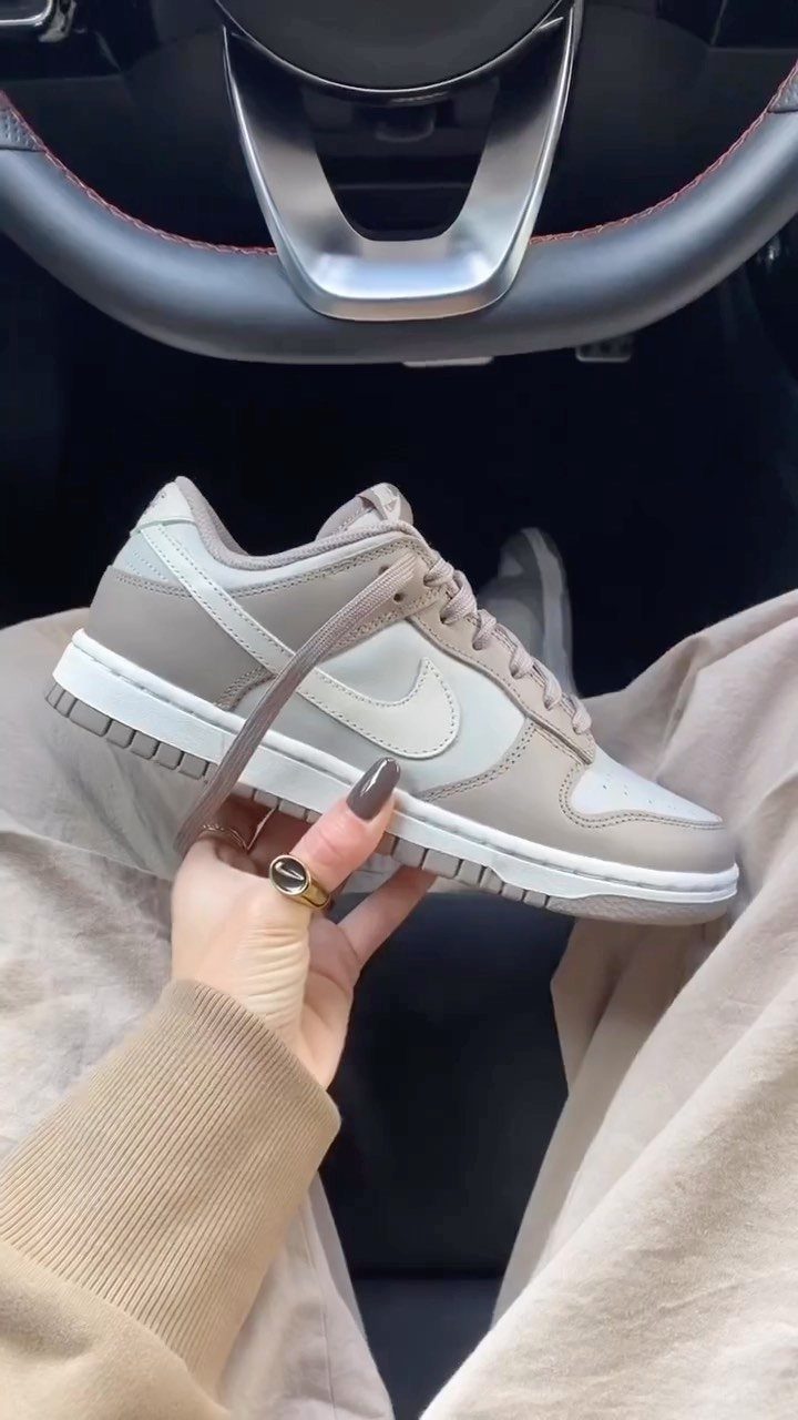 Beige Nike Dunk Low sneaker held by a hand inside a car.