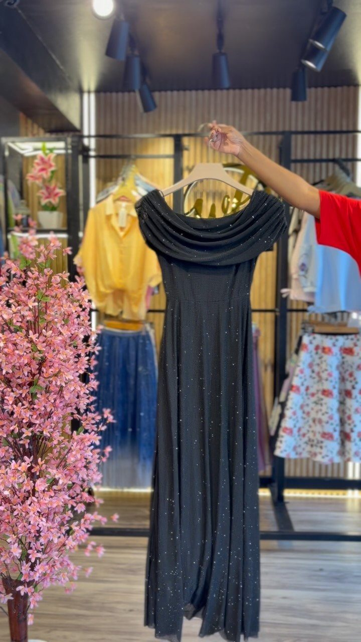 Black off-the-shoulder sparkling gown hanging in a boutique next to pink flowers