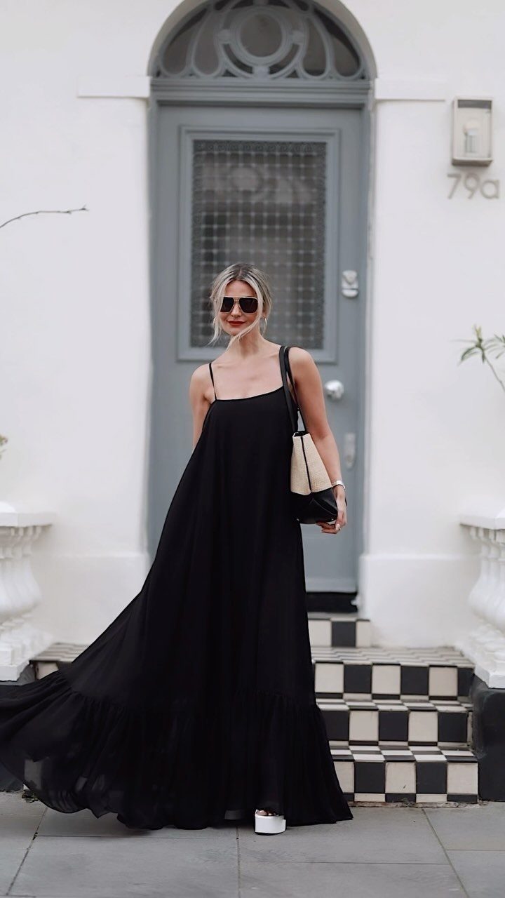 6 Black Dress Design Ideas for Formal and Wedding Looks 5 Woman in a long black maxi dress holding a beige and black raffia bag.