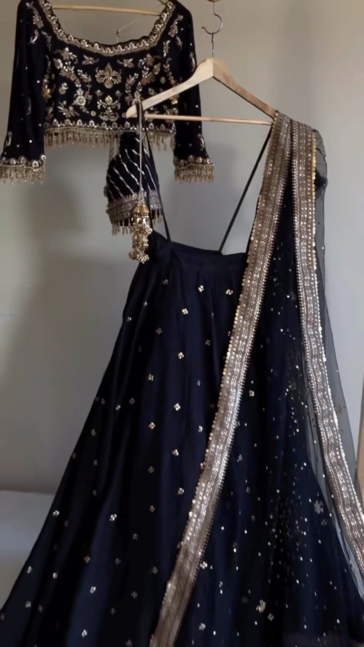 6 Black Dress Design Ideas for Formal and Wedding Looks 3 Black traditional Indian lehenga choli with gold embroidery hanging on wooden hangers.