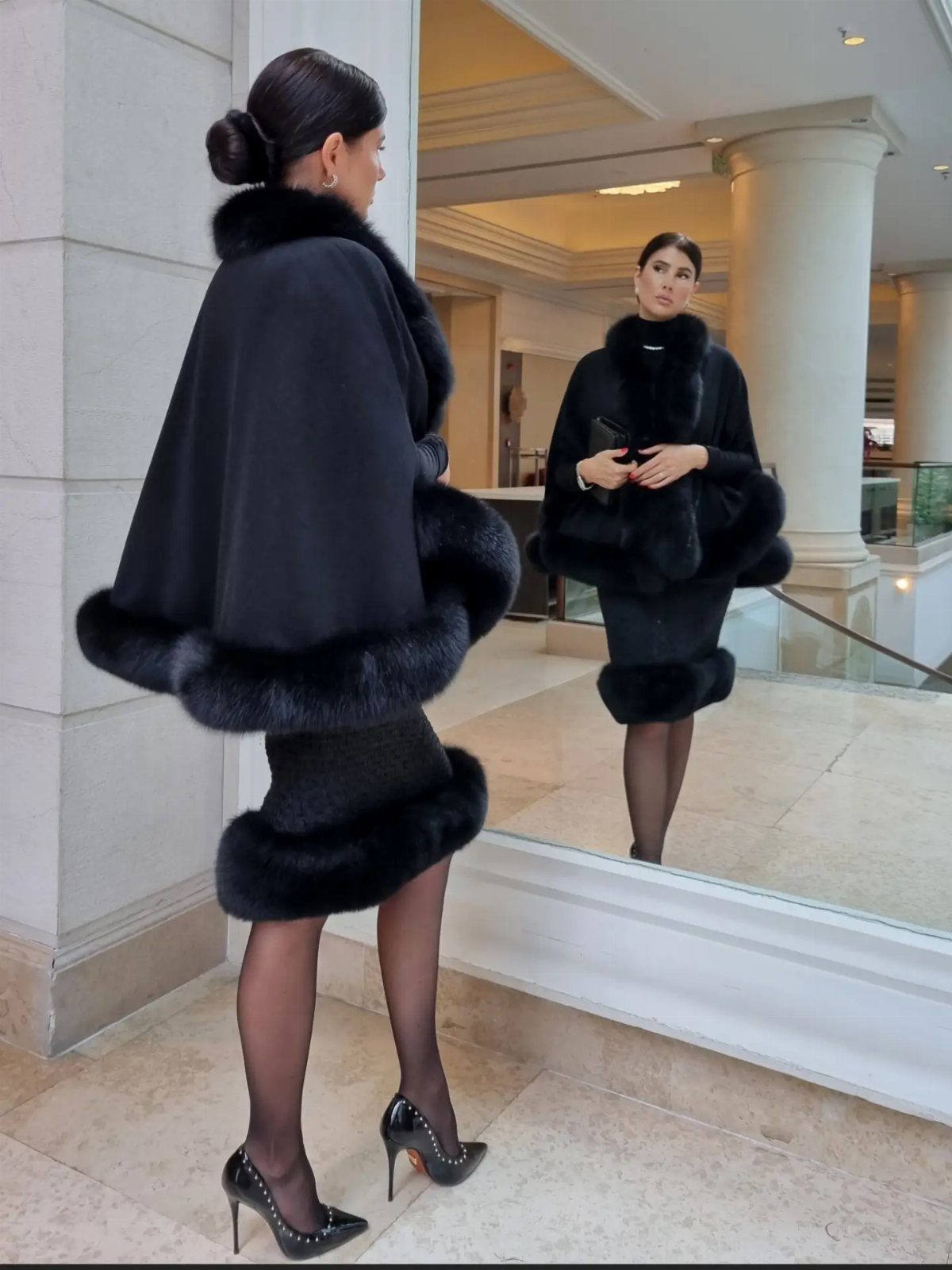 Woman in a black dress with fur trim and matching fur-trimmed cape.