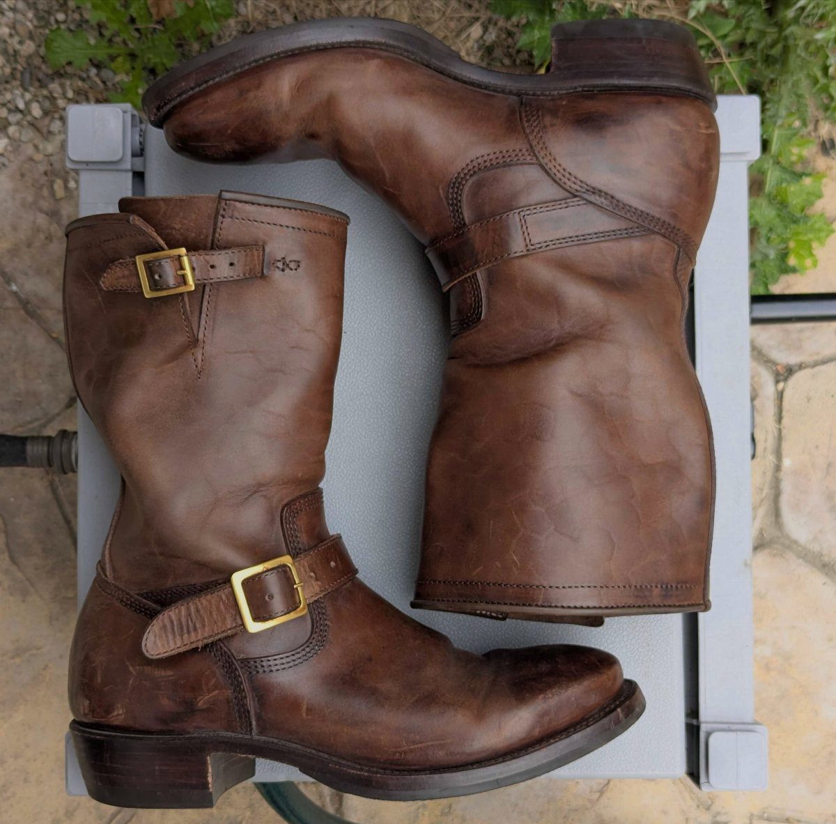 Black or Brown Boots for Every Outfit: 8 Ideas to Wear 2 Brown leather boots with gold buckles and a weathered patina on grey surface