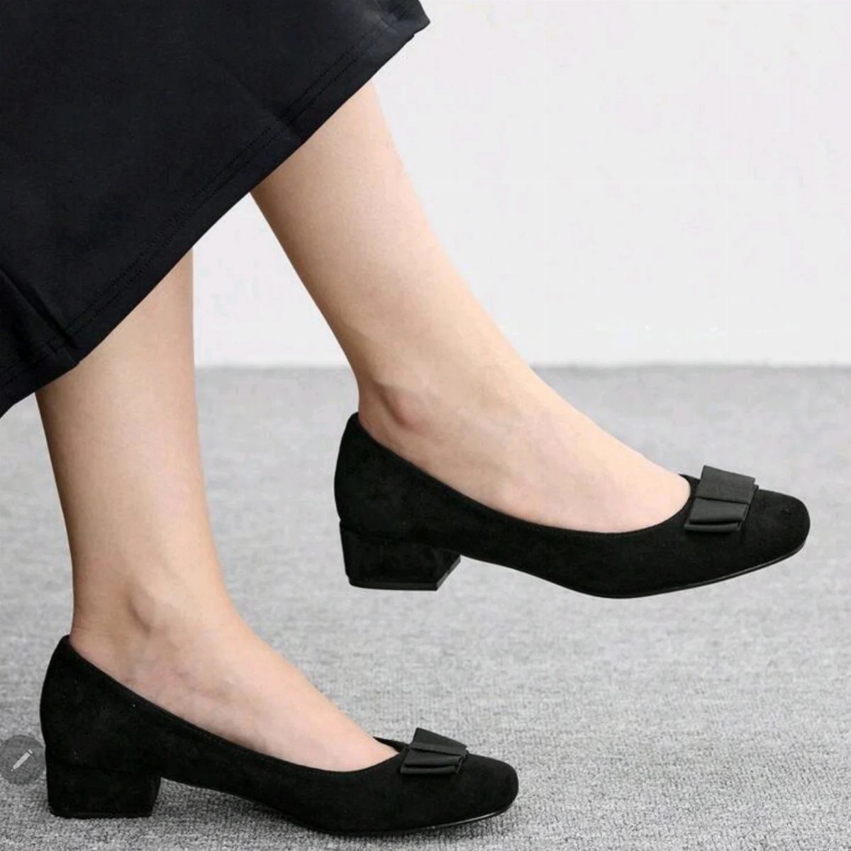 Black suede low block heel pumps with bows on a grey background