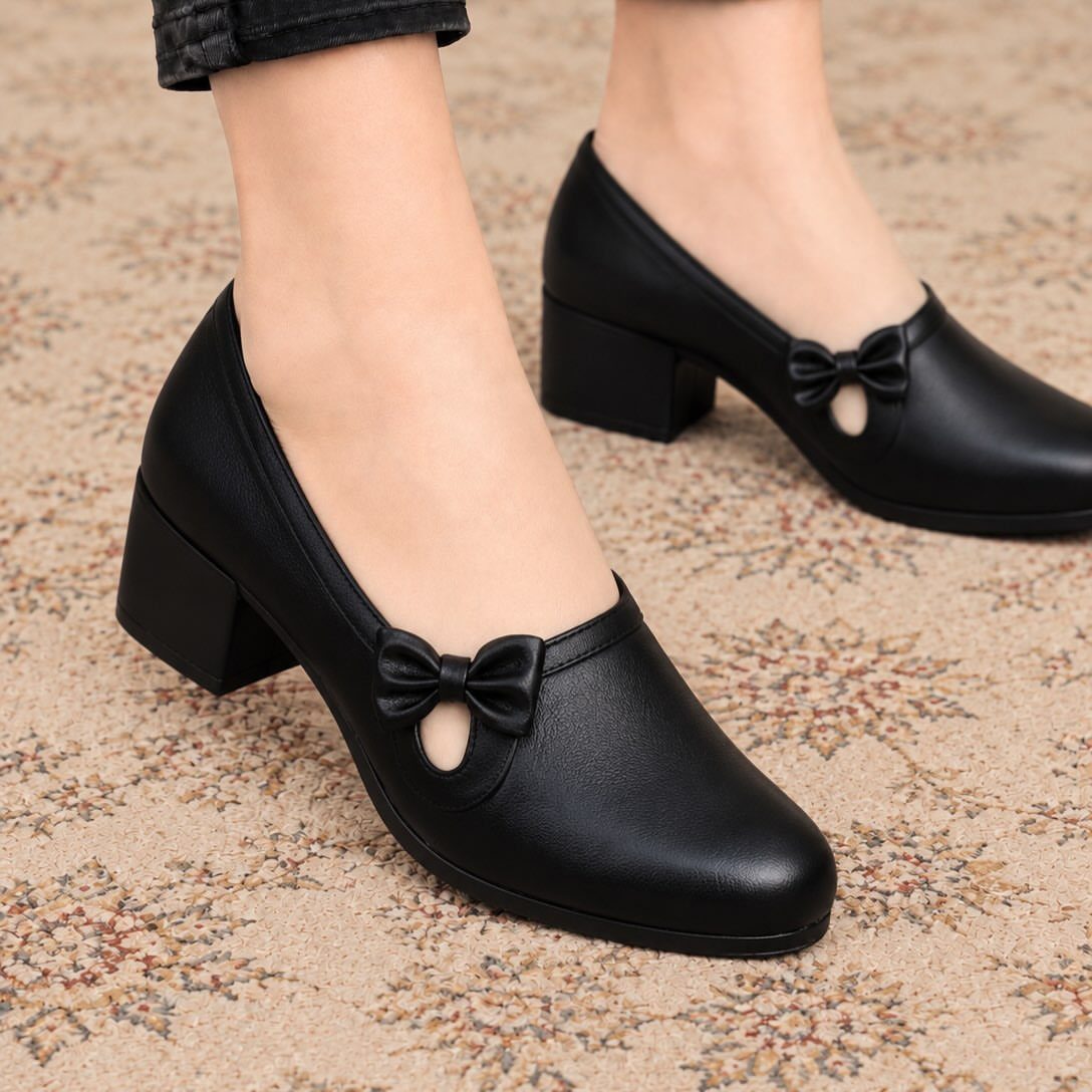 Black low-heel pumps with bow accents worn on a patterned beige carpet.
