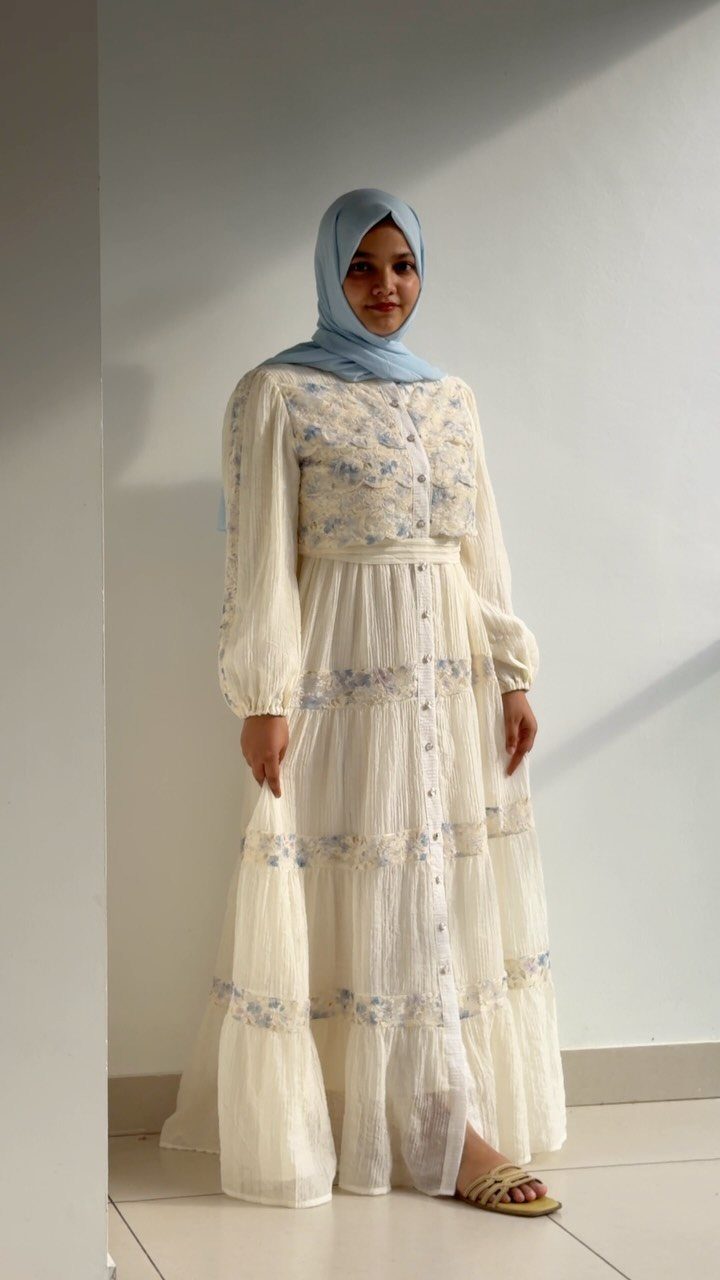 Boho Cream Dress Ideas: 7 Linen, Lace and Cotton Styles 1 Woman in blue hijab wearing a cream tiered maxi dress with floral embroidery.