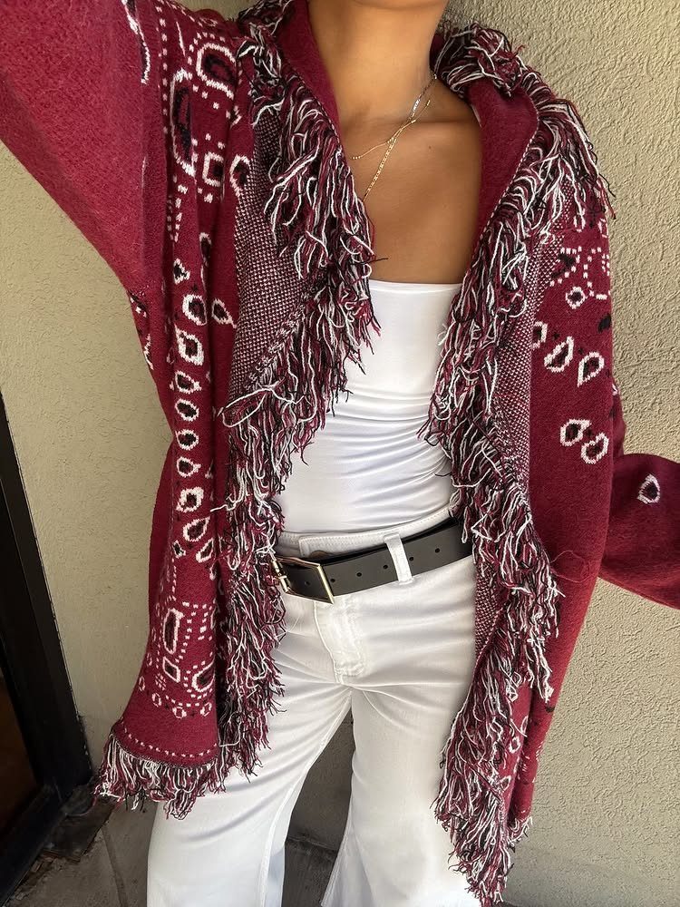Maroon patterned cardigan with long fringe trim worn over white clothing.