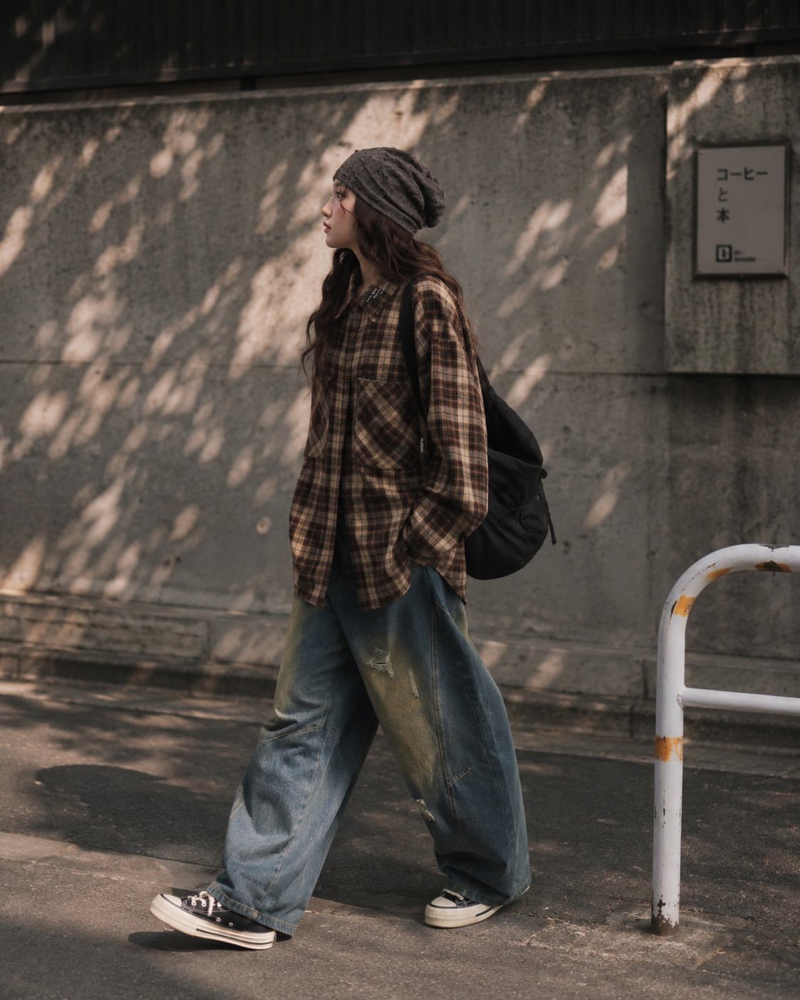 Person walking in a brown plaid shirt, baggy blue jeans, and grey beanie.