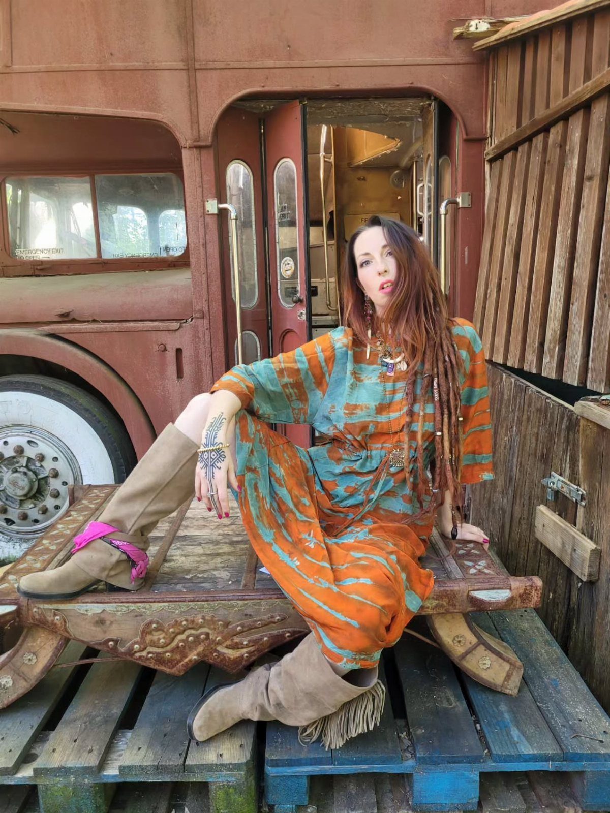 Woman in orange and blue tie-dye maxi dress sitting by vintage bus