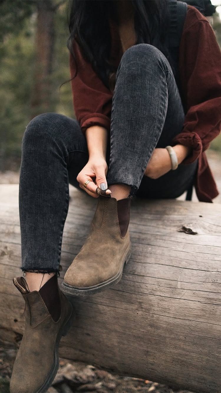 Brown suede Chelsea boots worn by a person sitting on a fallen log.
