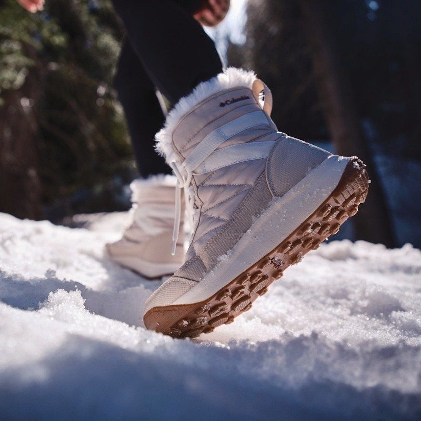 White quilted snow boots with fur trim walking through deep white snow.