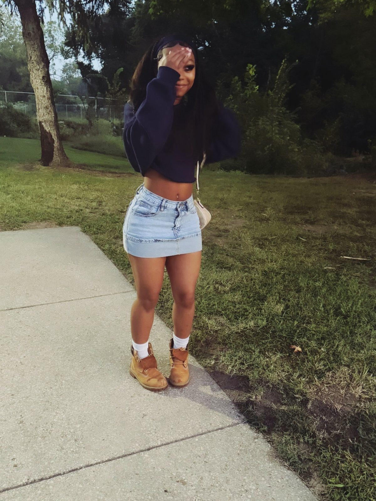 Young woman wearing a denim skirt and tan lace-up boots on a path.
