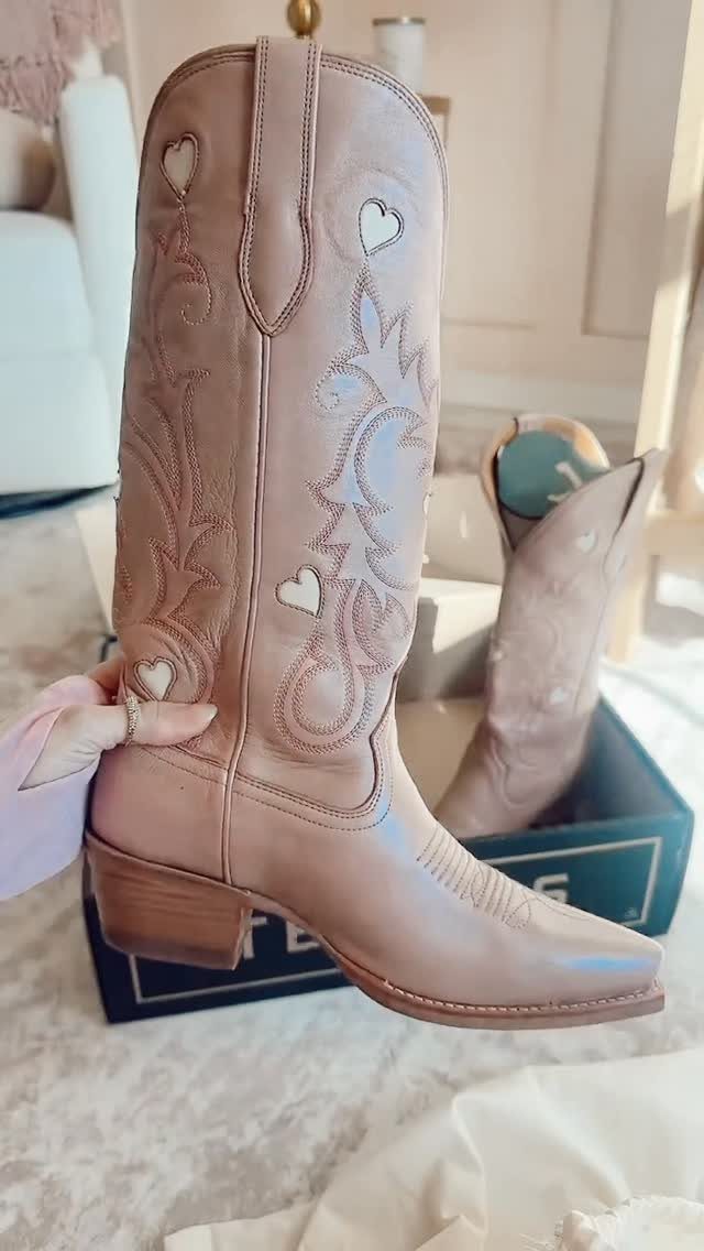 Light pink western boots with heart cutouts resting on a blue shoebox.