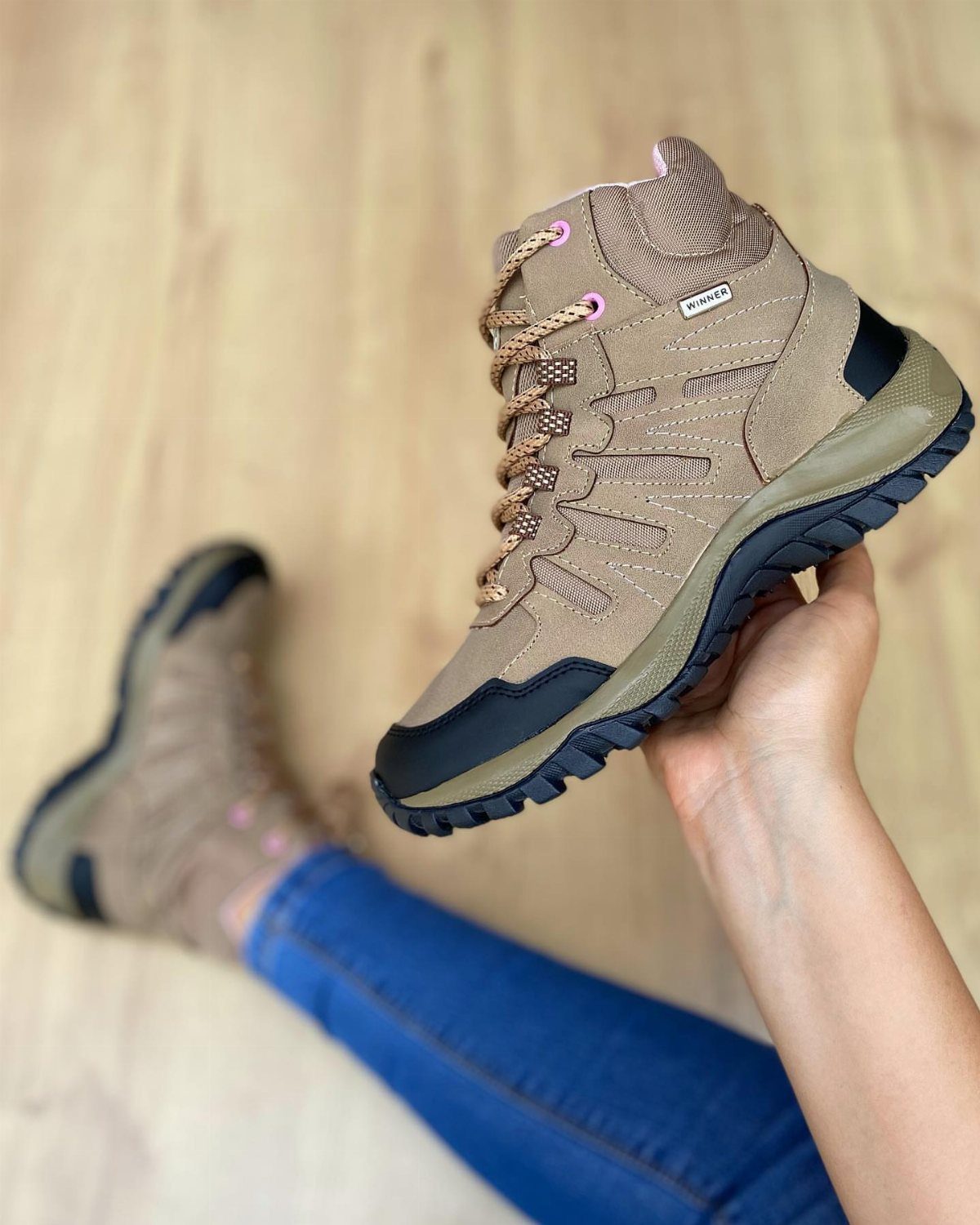 Tan and black waterproof hiking boots with pink laces held by a person.