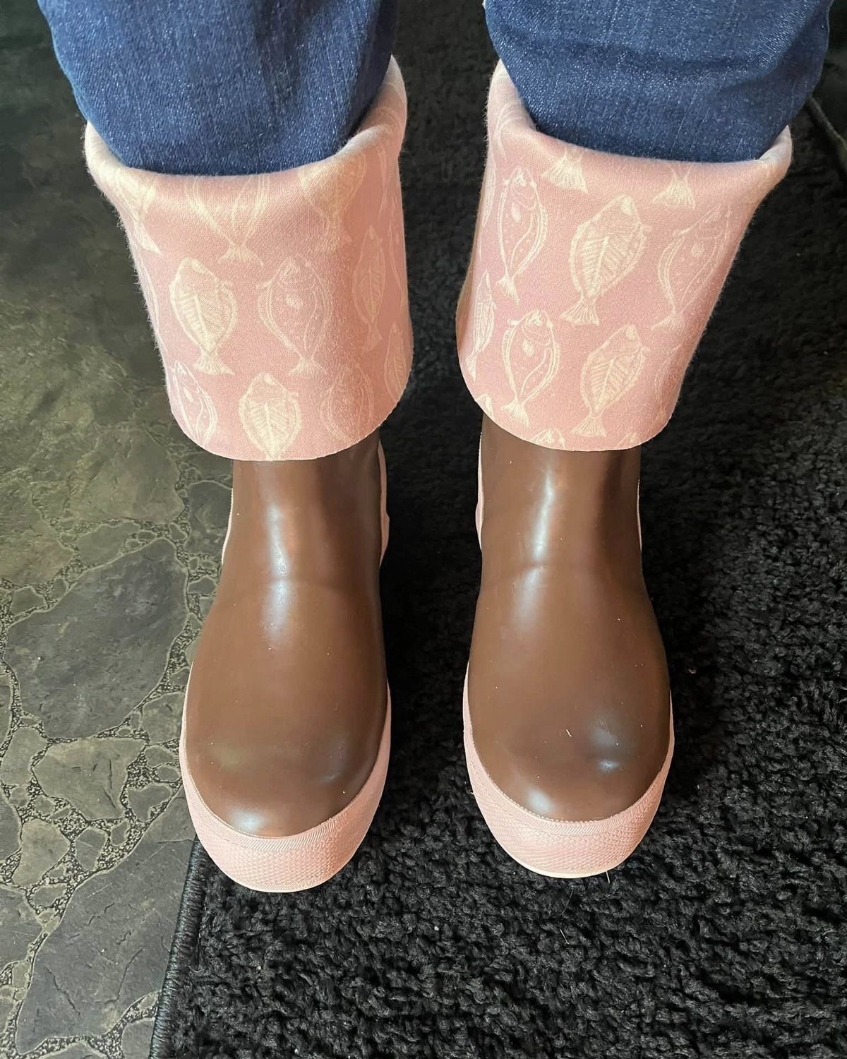 Brown waterproof boots with pink fish-patterned cuffs worn with blue denim jeans.