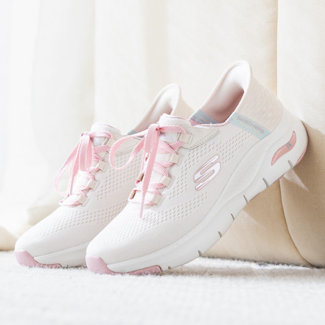White Skechers sneakers with pink laces on a soft white background