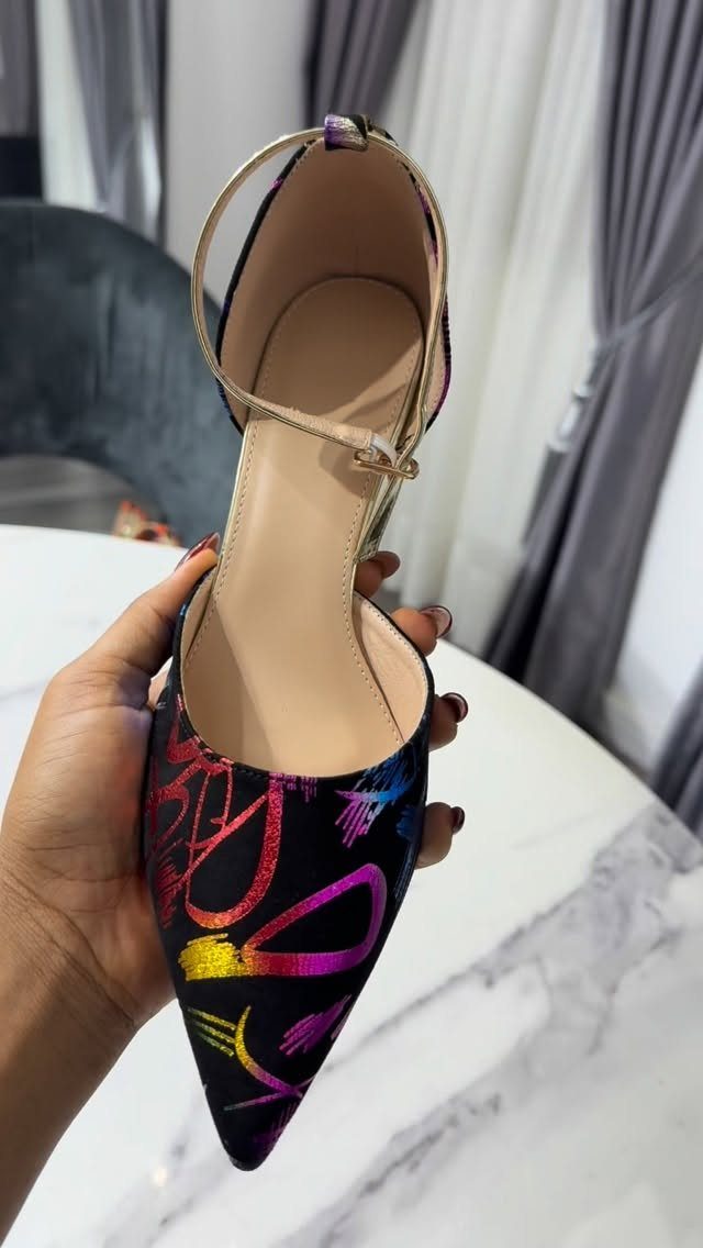 Black pointed-toe high heel with colorful abstract patterns held by a hand.