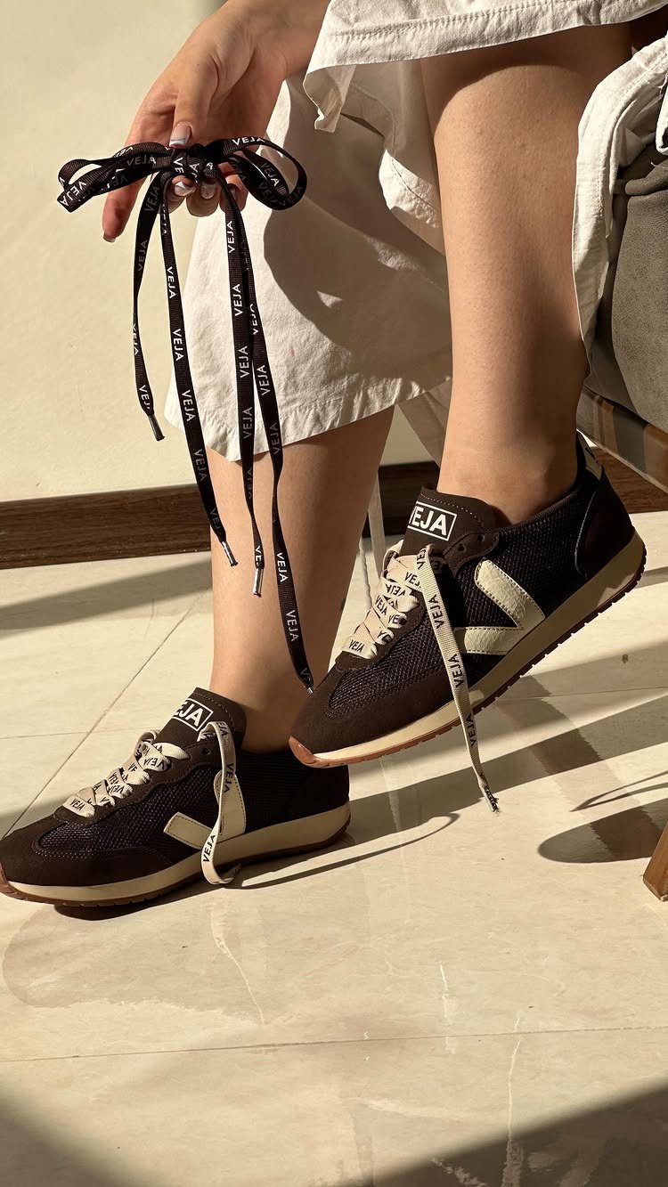 Dark brown Veja sneakers on a person's feet in a sunlit room