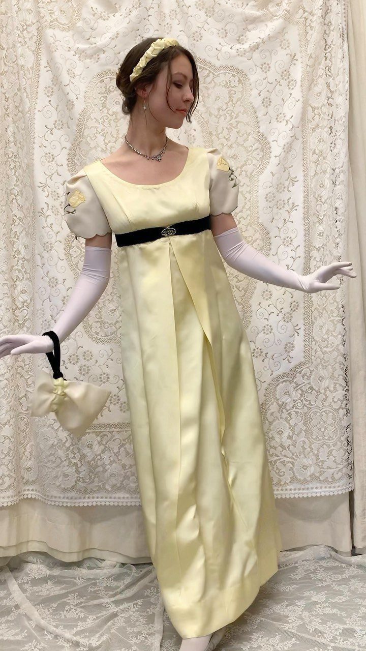 Woman in a pale yellow empire waist gown with white gloves and handbag.