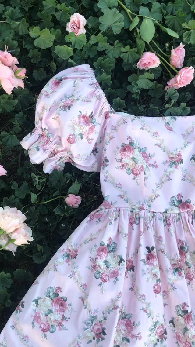 Light pink floral print dress with puffed sleeves resting on green foliage and roses.