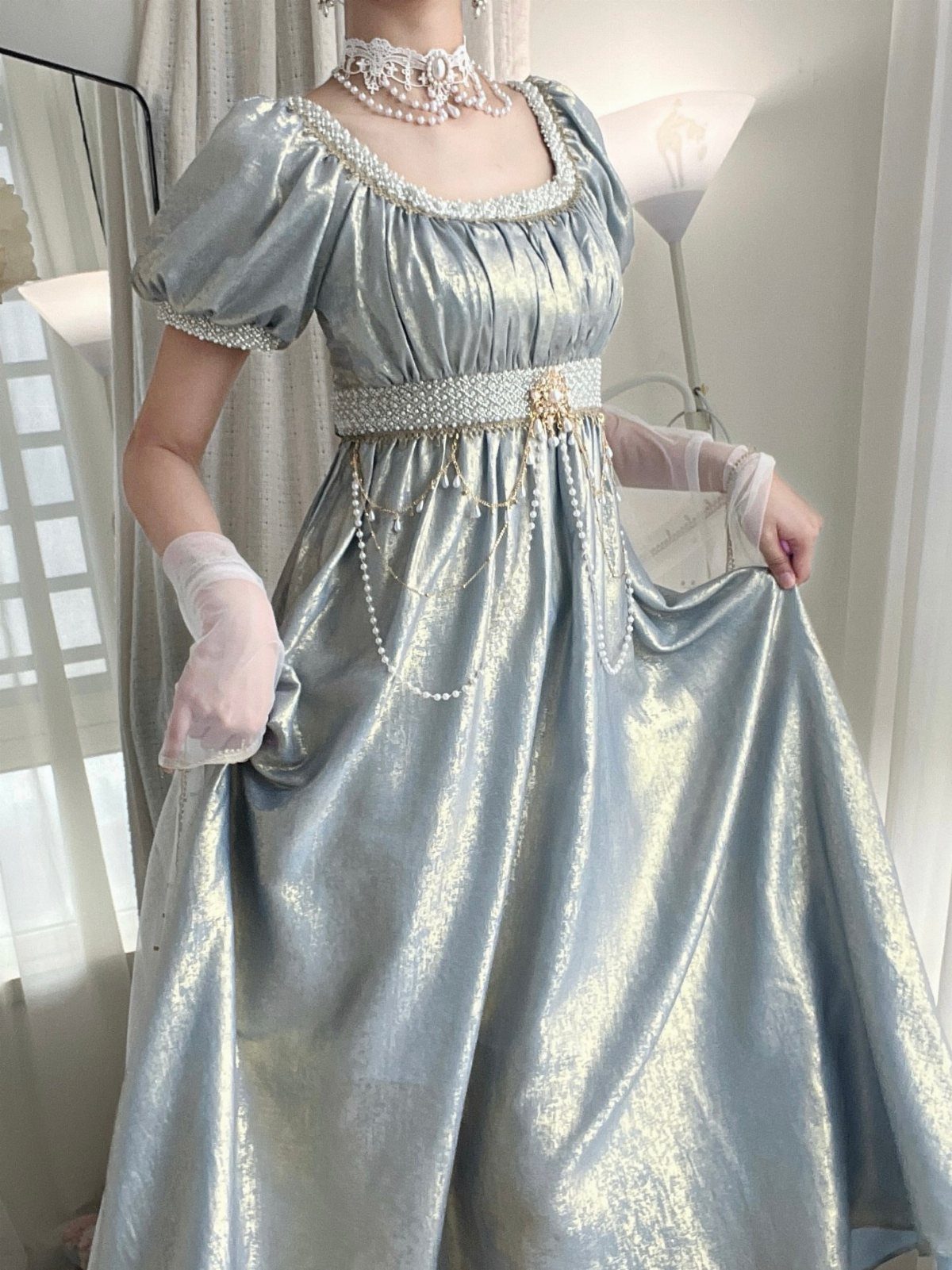 Person wearing a shimmering silver empire-waist gown with pearl accessories and white gloves.