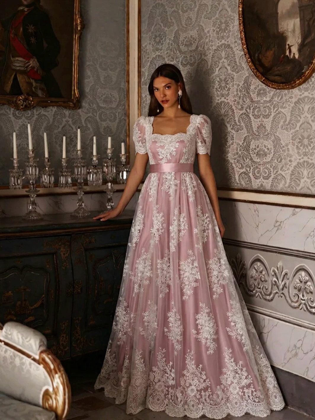 Woman in a pink empire waist dress with white floral lace embroidery and puffed sleeves.