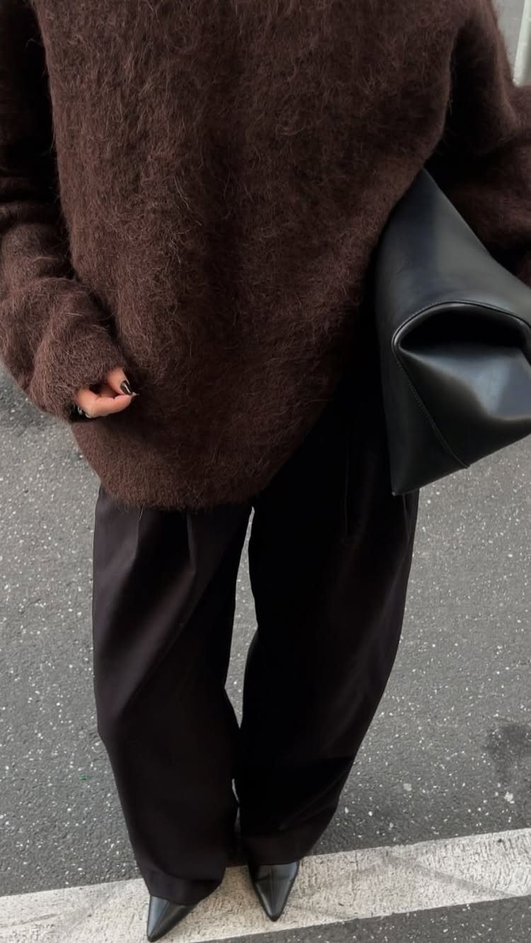 Person wearing a fuzzy chocolate brown sweater with black wide-leg trousers and clutch.