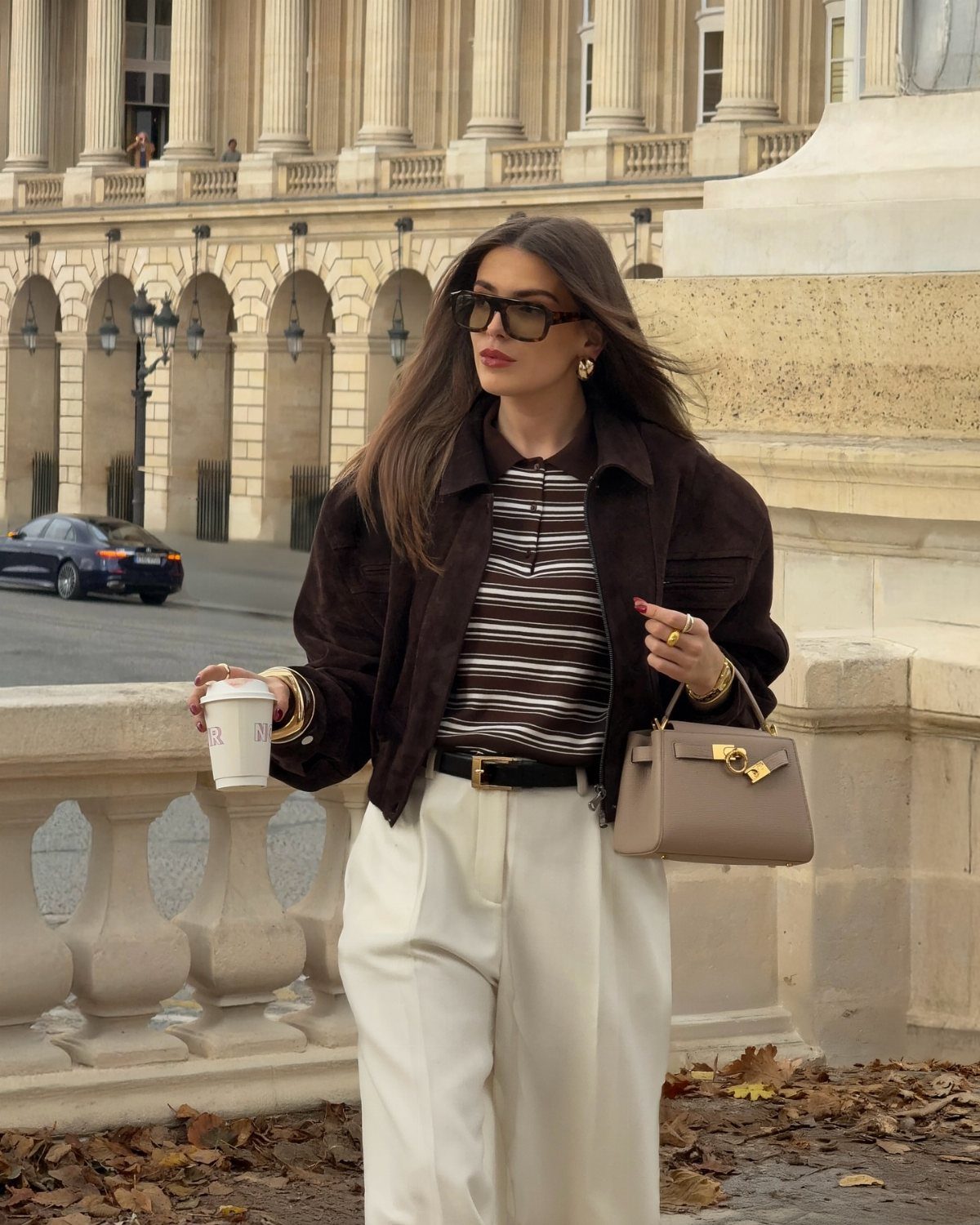 Woman in brown jacket and striped top with cream trousers holding a handbag