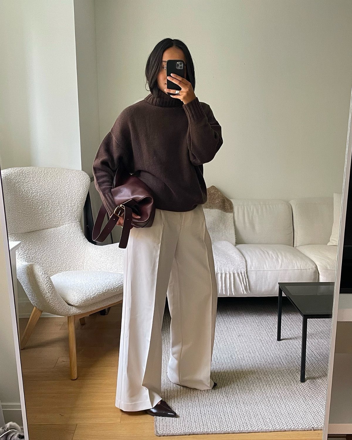 Woman wearing a chocolate brown turtleneck sweater with cream wide-leg trousers and handbag.