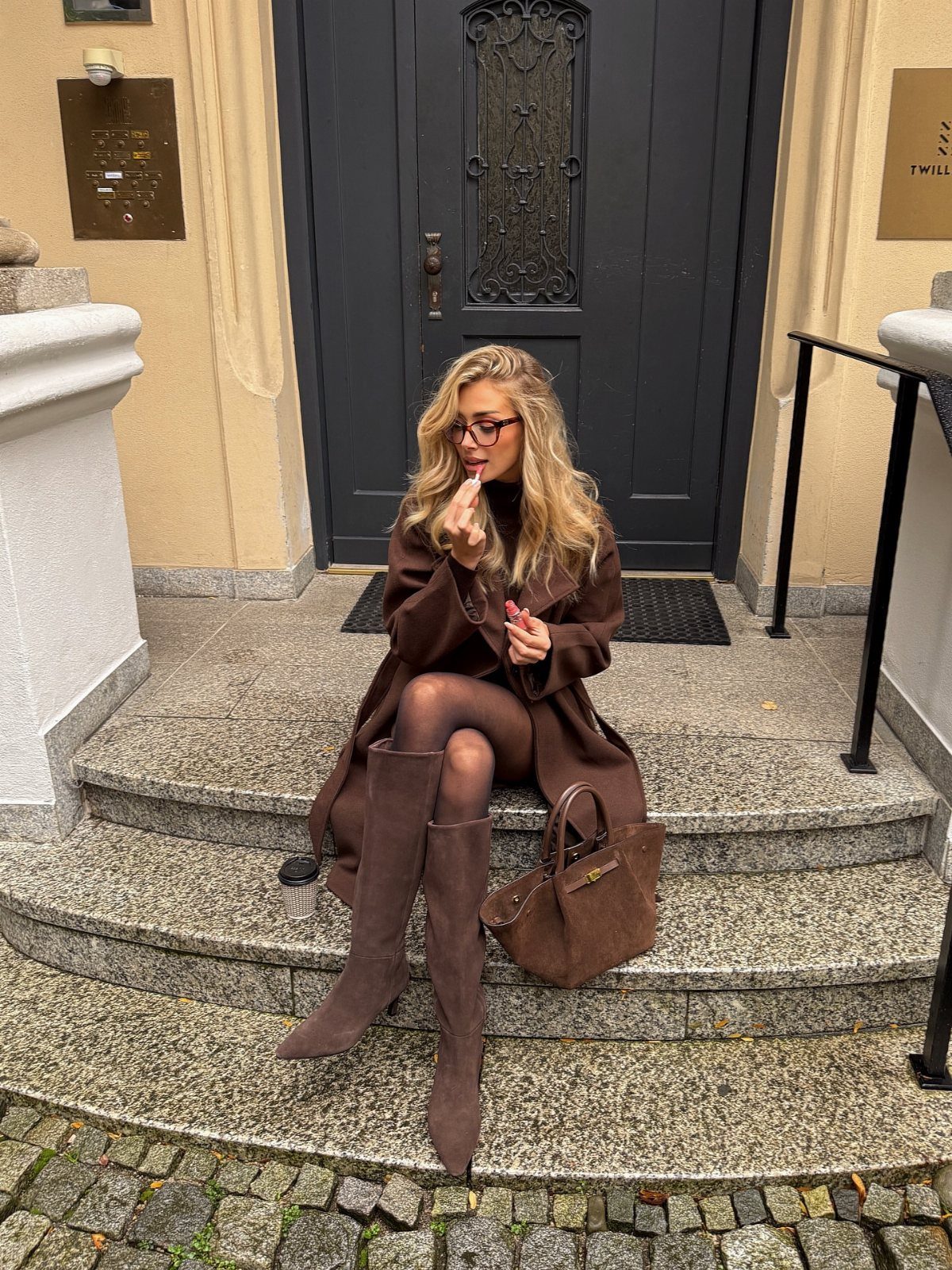 Woman in monochrome brown outfit sitting on stone steps with a brown handbag.